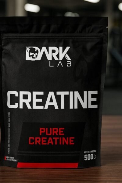 Pacote de creatina Dark Lab Pure Creatine de 500g sobre uma mesa de madeira, com o fundo mostrando uma academia moderna e desfocada. A embalagem preta com detalhes em vermelho e branco está em destaque no centro da imagem.